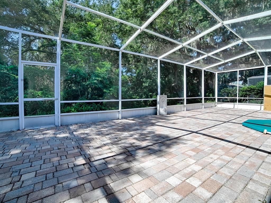A screened-in patio features paver flooring and views of surrounding trees — 830 OLD OAKS LANE, LEESBURG, FL