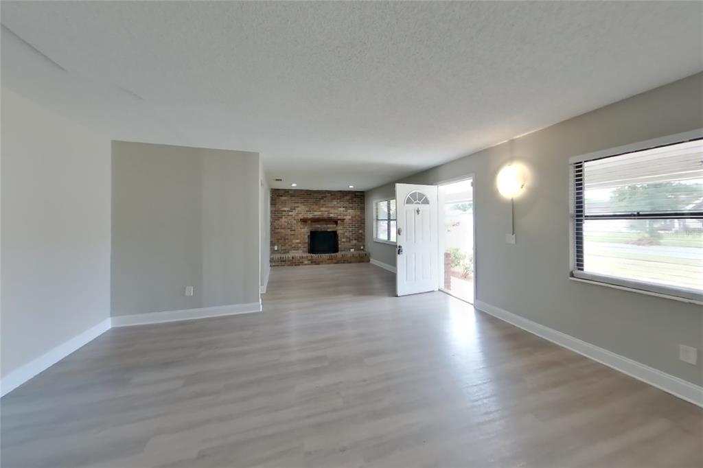 A living room with light wood-look flooring, gray walls, and a brick fireplace — 4905 LEPRECHAUN WAY, ORLANDO, FL
