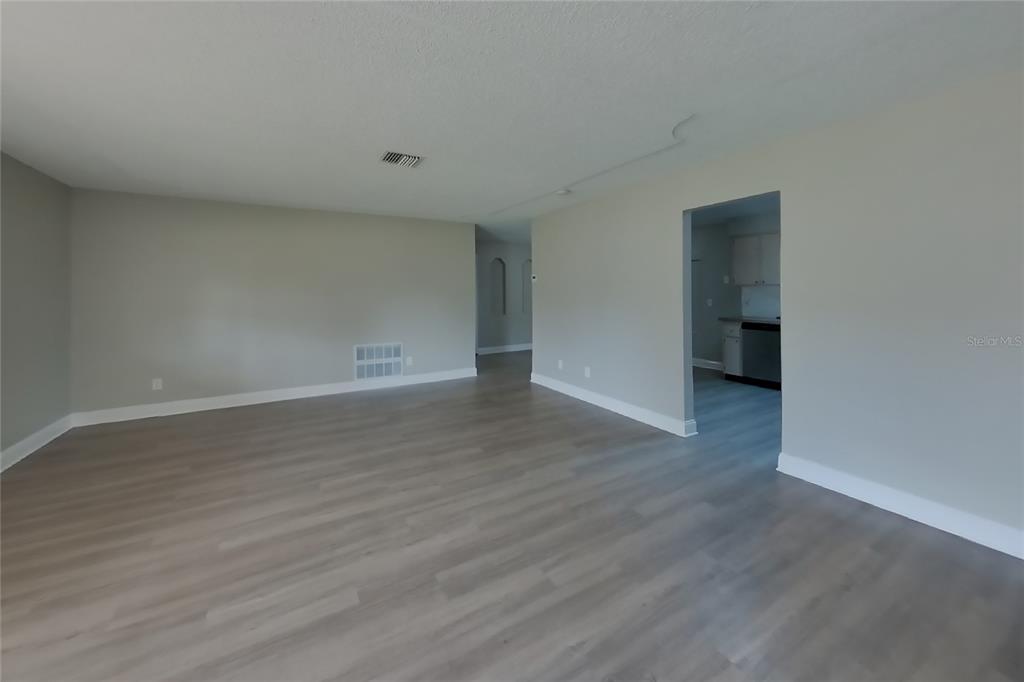 An empty room with light gray walls, wood-look flooring, and a doorway leading to a kitchen — 4905 LEPRECHAUN WAY, ORLANDO, FL