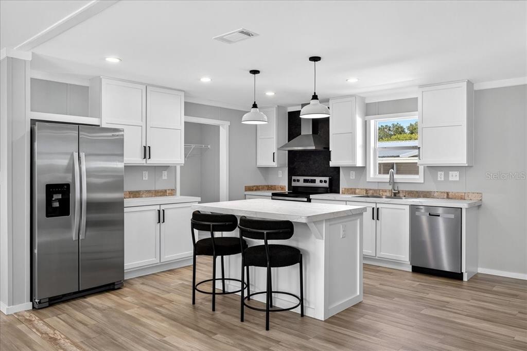 A modern kitchen features white cabinets, stainless steel appliances, a center island, and wood flooring — 24116 ARMADILLO ROAD, ASTOR, FL