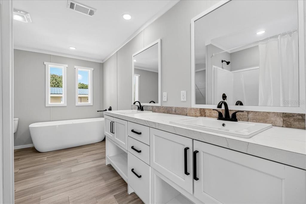 A modern bathroom features a double vanity, a freestanding tub, and light wood-look flooring — 24116 ARMADILLO ROAD, ASTOR, FL