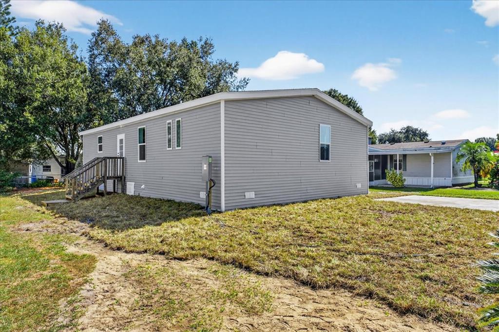 A gray manufactured home with a wooden staircase sits on a grassy lot — 24116 ARMADILLO ROAD, ASTOR, FL