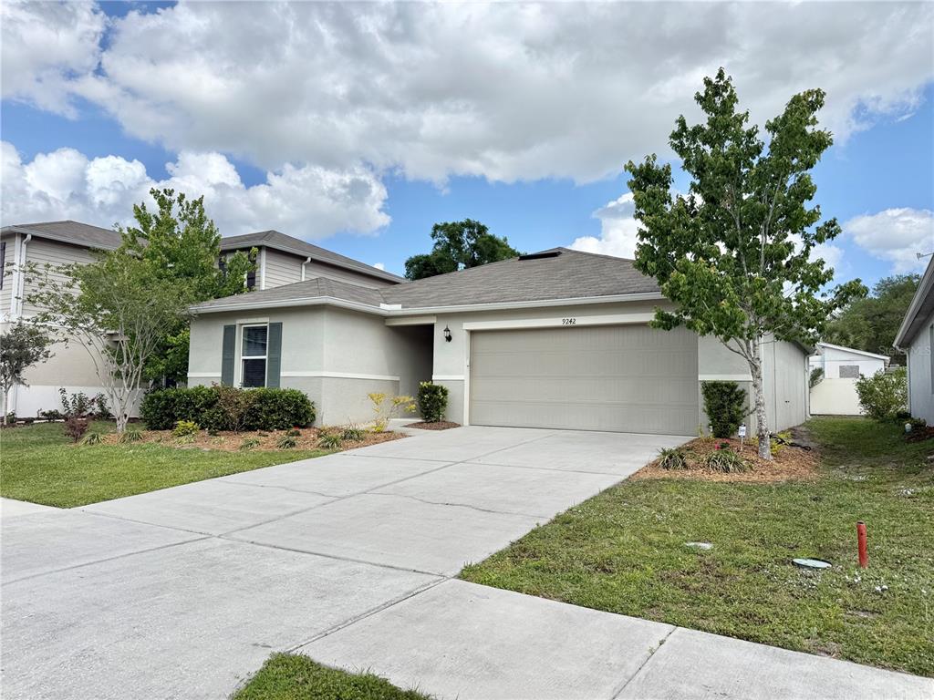 A single-story house with a beige stucco exterior, a two-car garage, and a concrete driveway — 9242 FREEDOM HILL DR, SEFFNER, FL