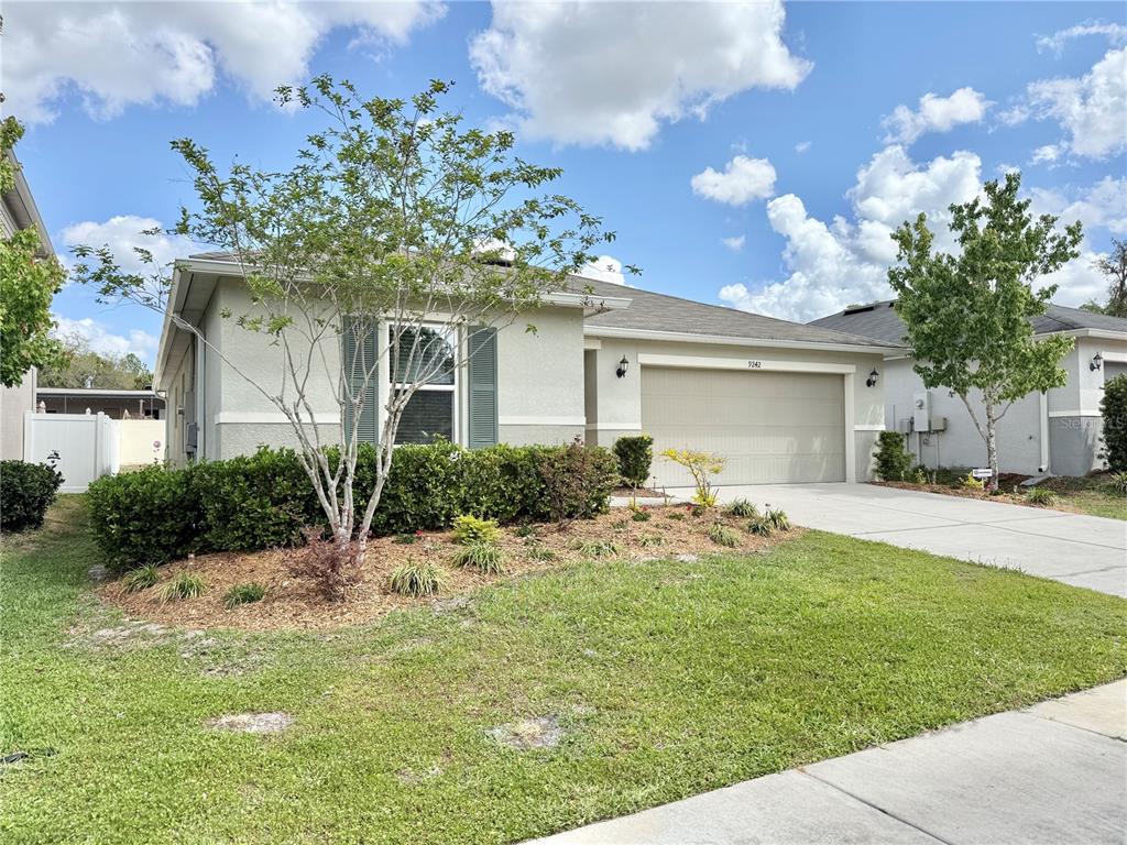 A single-story house with a beige stucco exterior, a two-car garage, and a landscaped yard — 9242 FREEDOM HILL DR, SEFFNER, FL