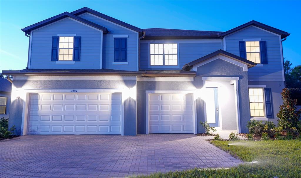 A two-story house with blue siding, a three-car garage, and a paved driveway at dusk — 2779 MATERA DRIVE, ST CLOUD, FL