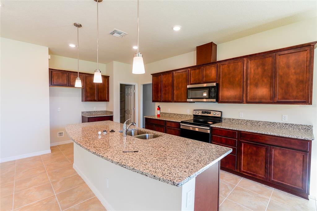 A kitchen features dark wood cabinets, granite countertops, a center island, and stainless steel appliances — 2779 MATERA DRIVE, ST CLOUD, FL