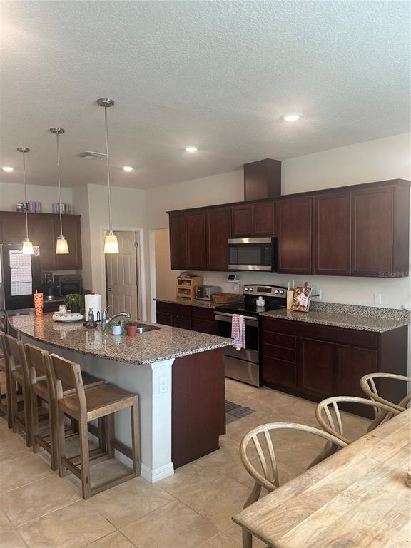A kitchen features dark wood cabinets, granite countertops, a center island, and stainless steel appliances — 2779 MATERA DRIVE, ST CLOUD, FL