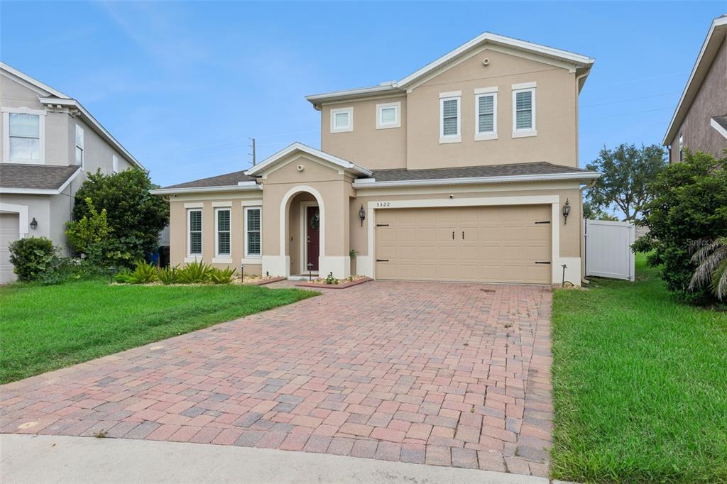 A two-story suburban house with a tan stucco exterior, a brick paver driveway, and a garage — 3522 HEART PINE LOOP, OCOEE, FL