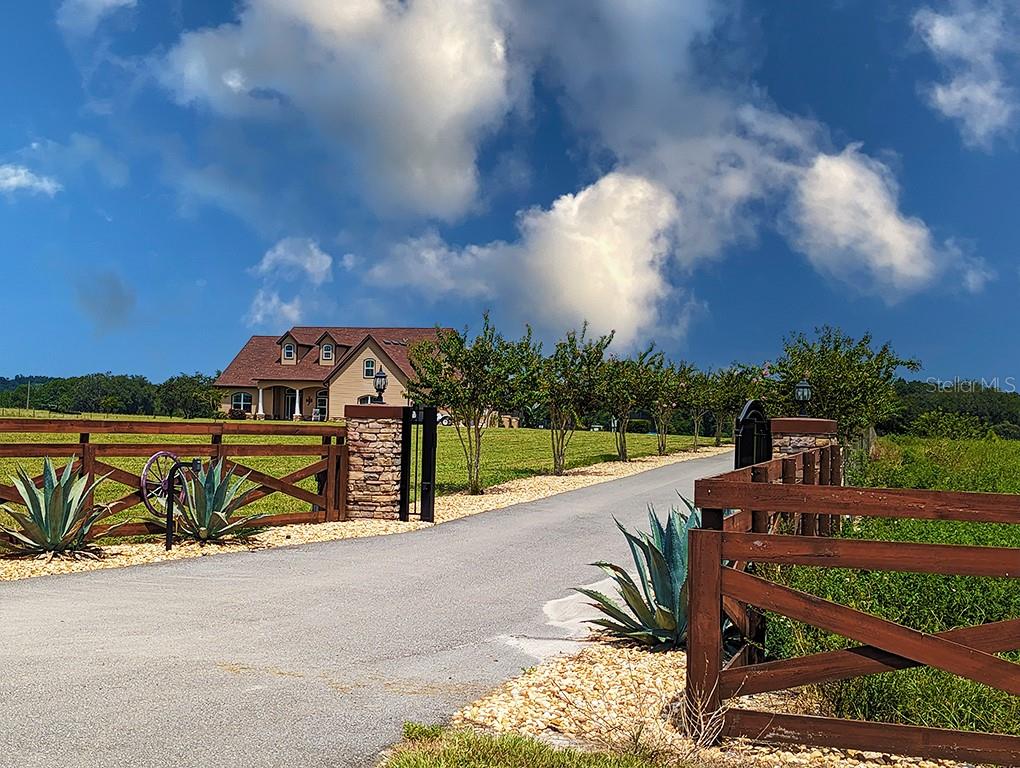 A paved driveway leads through a gated entrance toward a house with a brown roof — 19221 BAKER ROAD, UMATILLA, FL