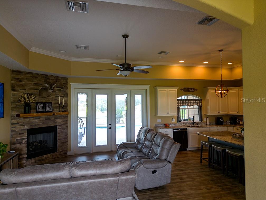 A living room with a stone fireplace, gray sofa, and an adjacent open-concept kitchen — 19221 BAKER ROAD, UMATILLA, FL