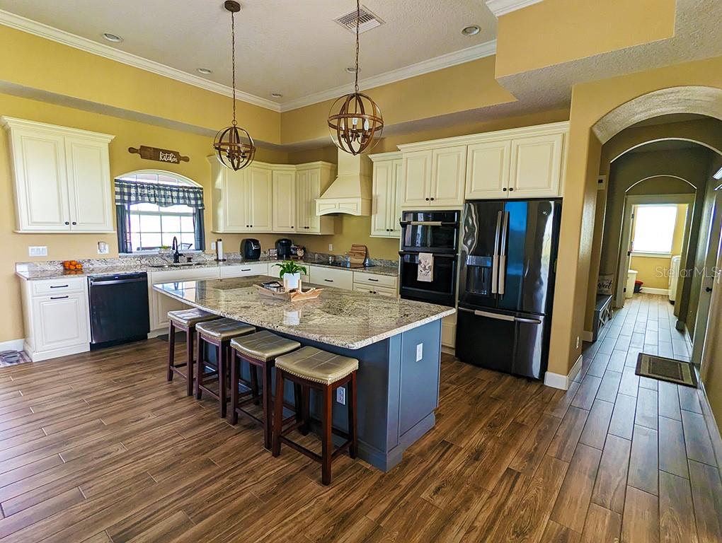 A kitchen features white cabinets, a blue island with bar stools, and wood-look tile flooring — 19221 BAKER ROAD, UMATILLA, FL