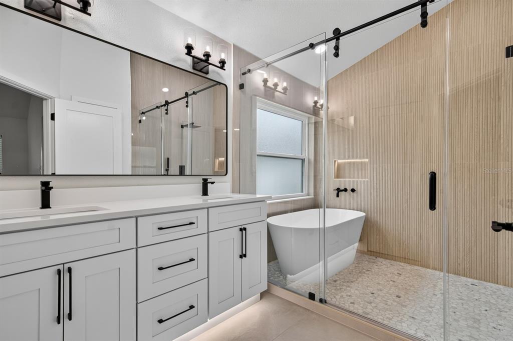 A modern bathroom features a white double vanity, a freestanding tub, and a glass-enclosed shower — 7737 MARBELLA CREEK AVENUE, TAMPA, FL