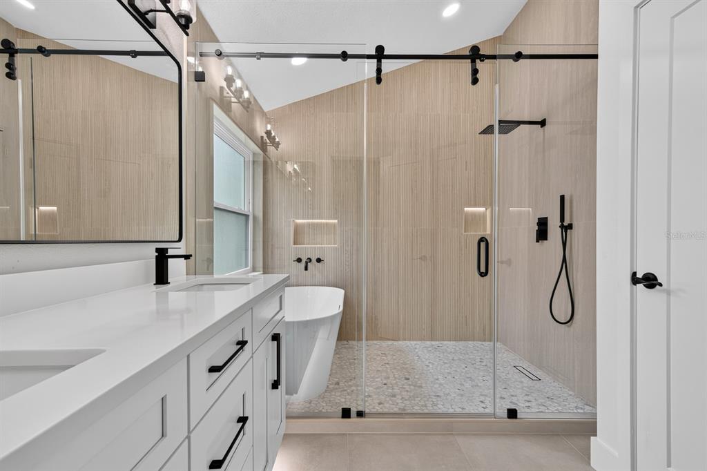 A modern bathroom features a white double vanity, a freestanding tub, and a glass-enclosed shower — 7737 MARBELLA CREEK AVENUE, TAMPA, FL