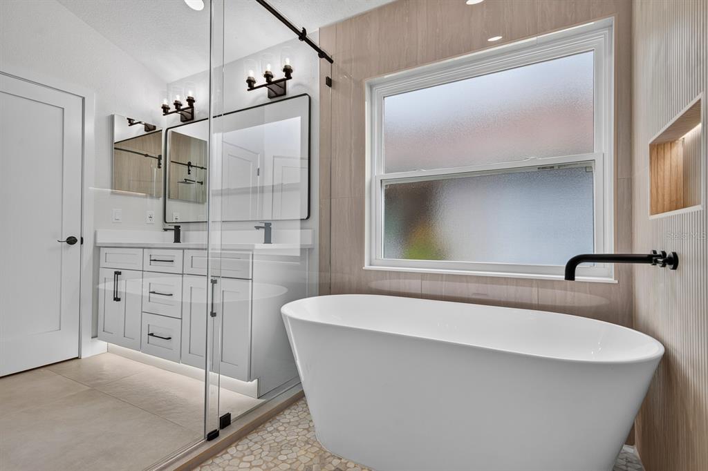 A modern bathroom features a freestanding white tub, a glass-enclosed shower, and a double vanity — 7737 MARBELLA CREEK AVENUE, TAMPA, FL