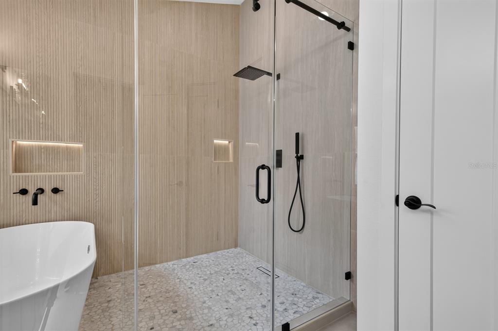 A modern bathroom features a freestanding tub, a glass-enclosed shower, and light wood-slatted walls — 7737 MARBELLA CREEK AVENUE, TAMPA, FL