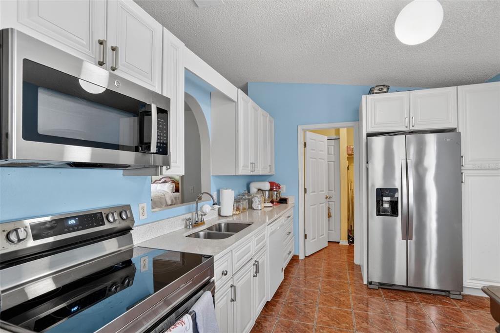 A kitchen with white cabinets, stainless steel appliances, light countertops, and orange tile flooring — 6820 POMEROY CIRCLE, ORLANDO, FL