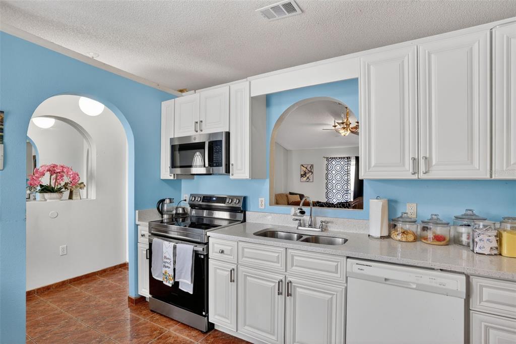 A kitchen features white cabinets, stainless steel appliances, light countertops, and blue walls with arches — 6820 POMEROY CIRCLE, ORLANDO, FL