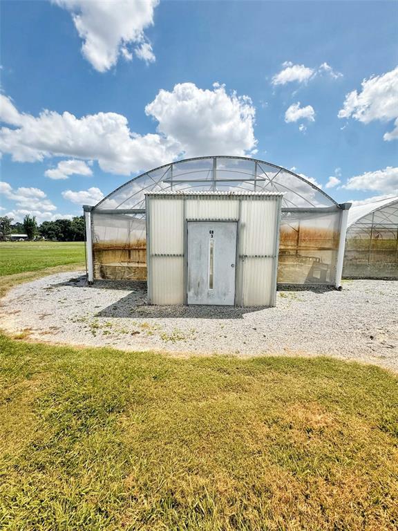 A greenhouse with a central metal door stands on a gravel lot under a sky — 612 MORGAN ROAD, WINTER HAVEN, FL