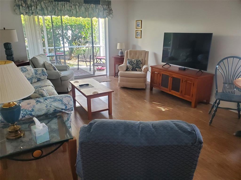 A living room features floral furniture, a television on a wooden stand, and sliding glass doors — 1232 CAPRI ISLES BOULEVARD UNIT 48, VENICE, FL