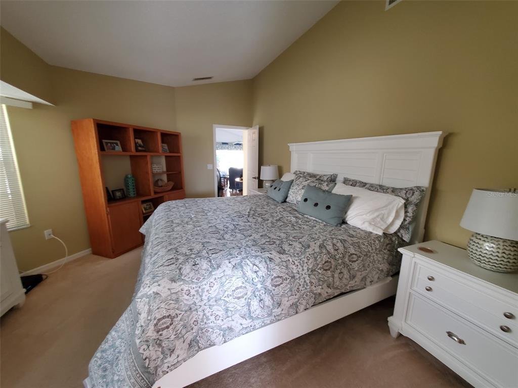 A bedroom features a white bed frame, patterned bedding, a wooden bookshelf, and white nightstands — 1232 CAPRI ISLES BOULEVARD UNIT 48, VENICE, FL