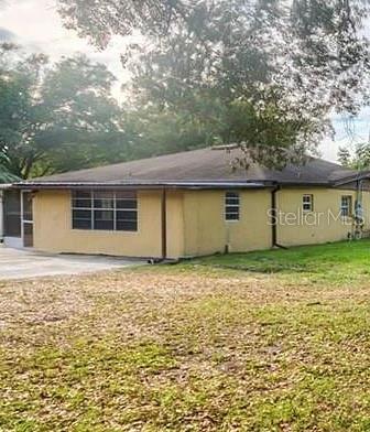 A side view of a yellow, single-story house with a dark roof and large trees — 1 S AURORA DRIVE, APOPKA, FL