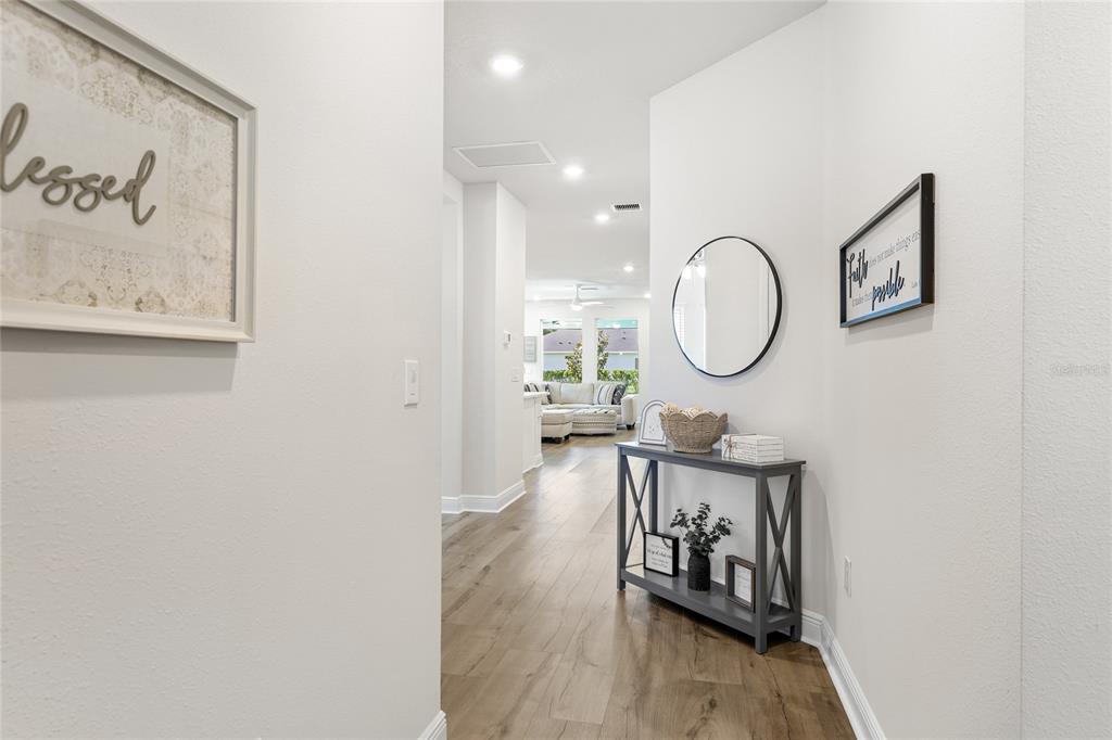 A hallway with wood-look flooring leads to a living area featuring a console table — 11805 CATAWBA COVE, PARRISH, FL