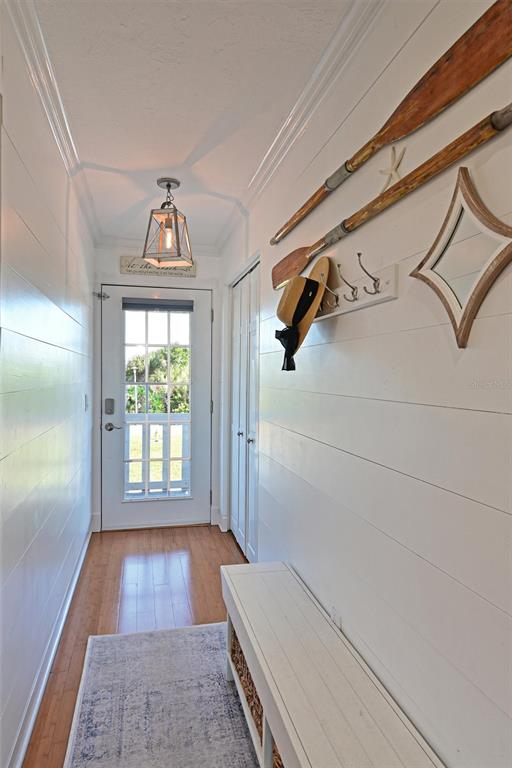 A hallway with white shiplap walls, a wooden bench, and nautical decor leads to a door — 10313 WATERBIRD WAY, BRADENTON, FL