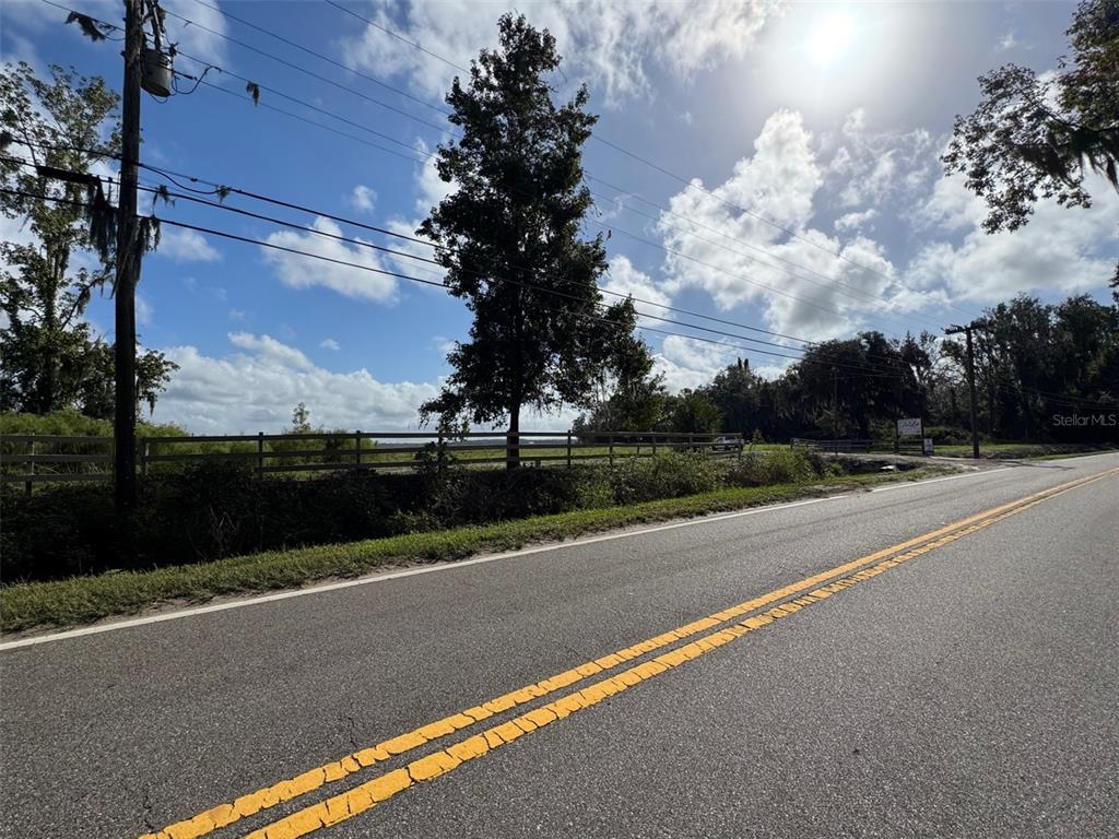 A paved road runs alongside a fenced grassy lot with trees under a cloudy sky — 380 CR 13 S STREET, ST AUGUSTINE, FL