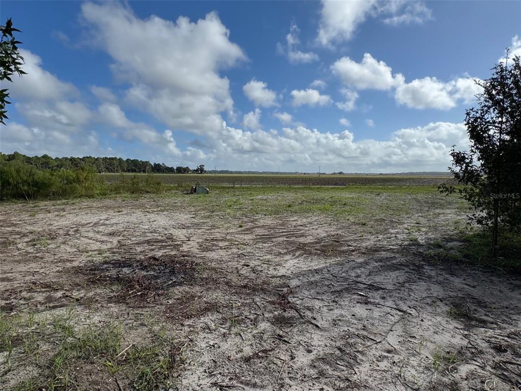 A flat, sandy, cleared lot overlooks a large open field under a cloudy blue sky — 380 CR 13 S STREET, ST AUGUSTINE, FL