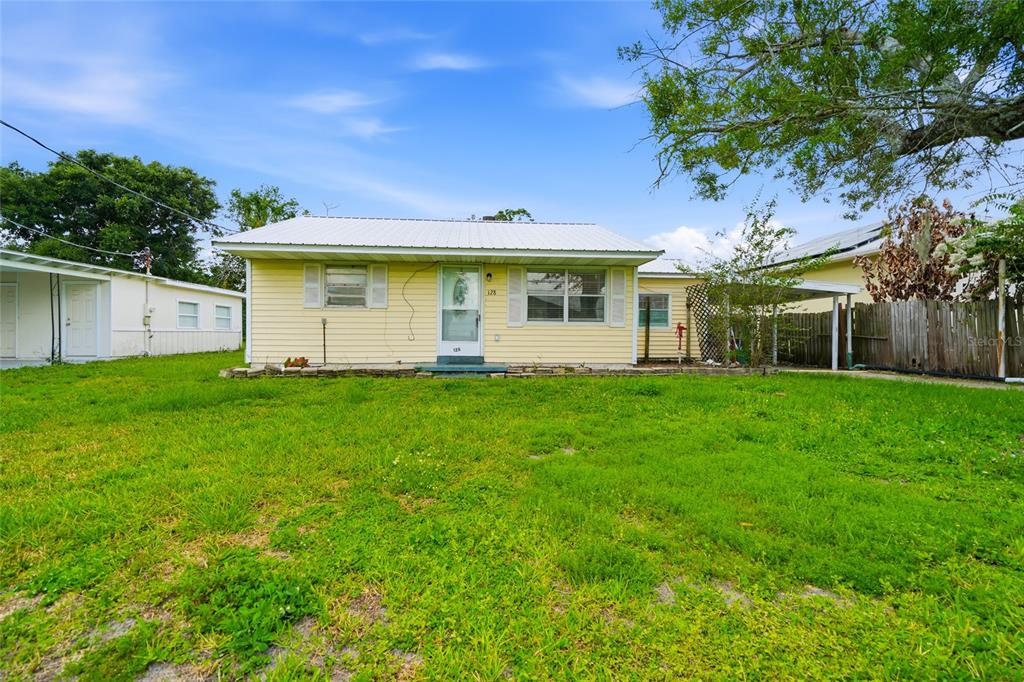 A single-story yellow house with a white metal roof sits on a grassy lot — 128 NW 10TH DRIVE, MULBERRY, FL