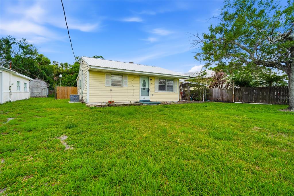 A yellow, single-story house with a metal roof stands on a grassy lot — 128 NW 10TH DRIVE, MULBERRY, FL