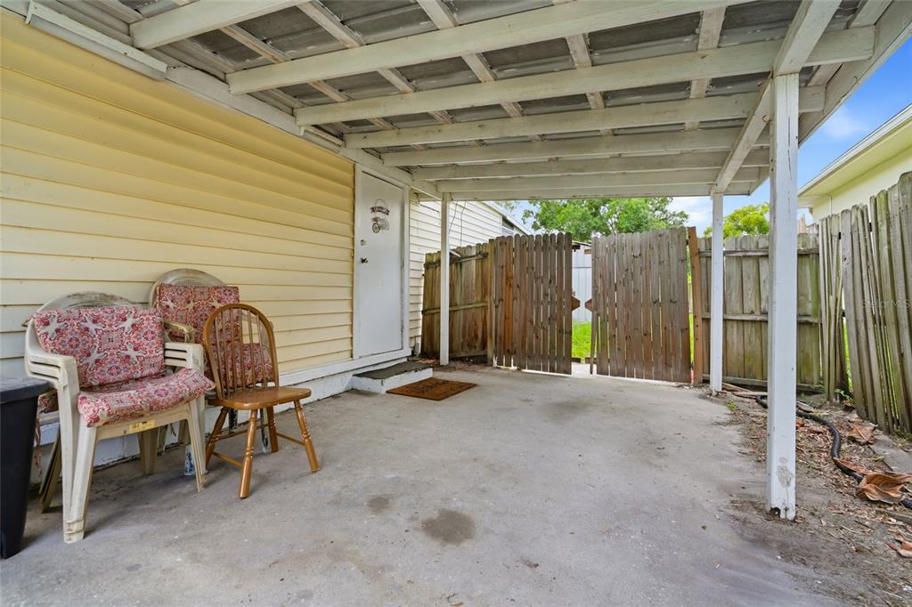 A covered concrete patio features yellow siding, a white door, and a wooden fence — 128 NW 10TH DRIVE, MULBERRY, FL