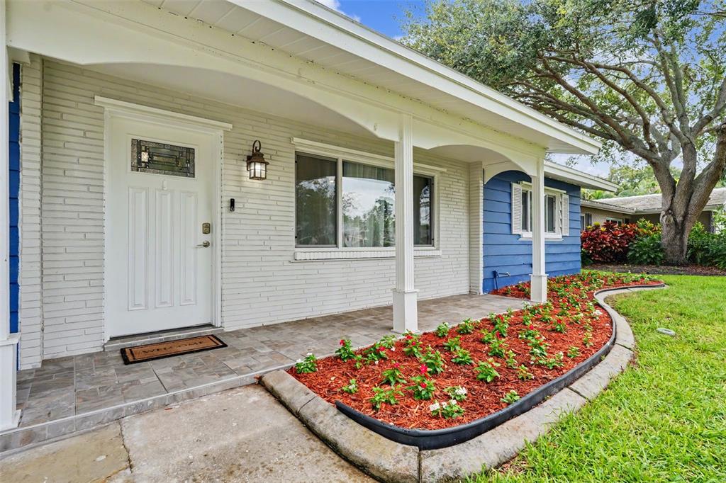 A white brick house exterior features a covered porch, a front door, and a flowerbed — 1340 WILLIAMS DRIVE, CLEARWATER, FL