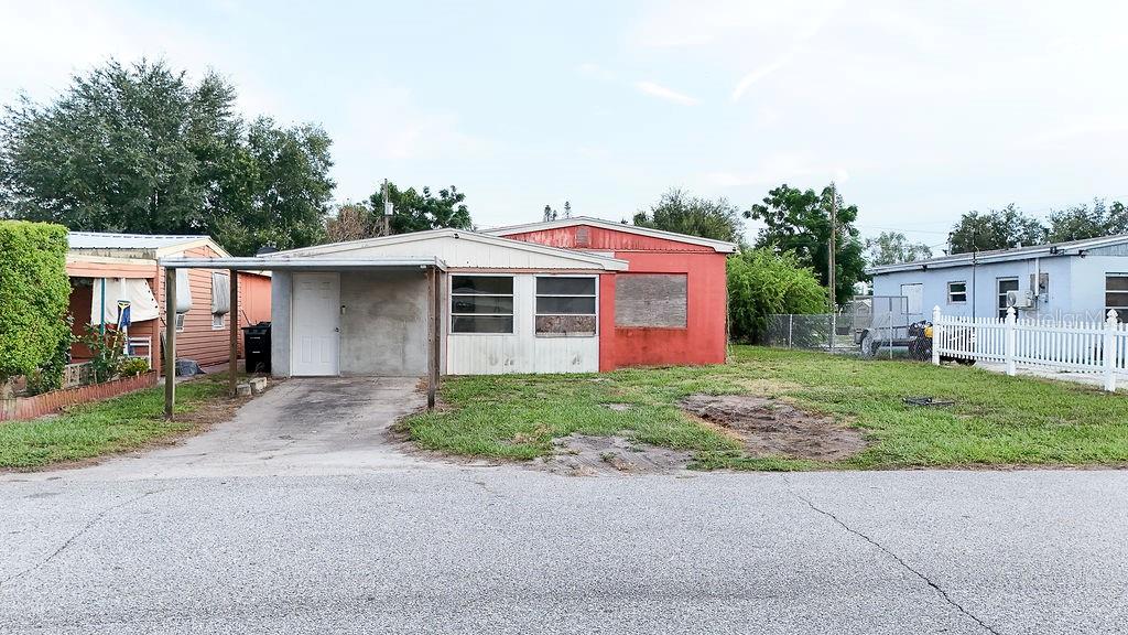 A single-story house with a red exterior, a carport, and boarded-up windows — 99 YALE AVENUE, FROSTPROOF, FL