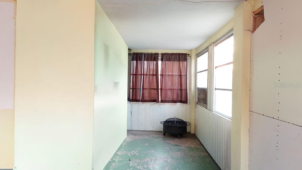 A sunroom with a green painted floor, brown curtains, and unfinished drywall walls — 99 YALE AVENUE, FROSTPROOF, FL