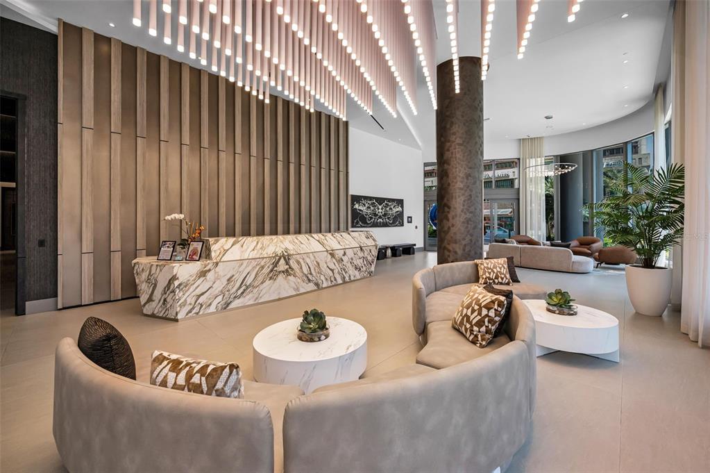 A modern lobby features a marble reception desk, curved seating, and hanging cylindrical light fixtures — 275 1ST AVENUE S UNIT 3503, ST PETERSBURG, FL