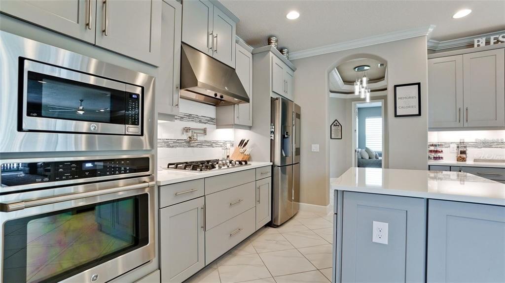 A modern kitchen features gray cabinets, stainless steel appliances, white countertops, and tile flooring — 5738 HYDRANGEA CIRCLE, SARASOTA, FL