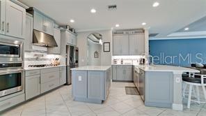 A modern kitchen features light gray cabinetry, a central island, and stainless steel appliances — 5738 HYDRANGEA CIRCLE, SARASOTA, FL