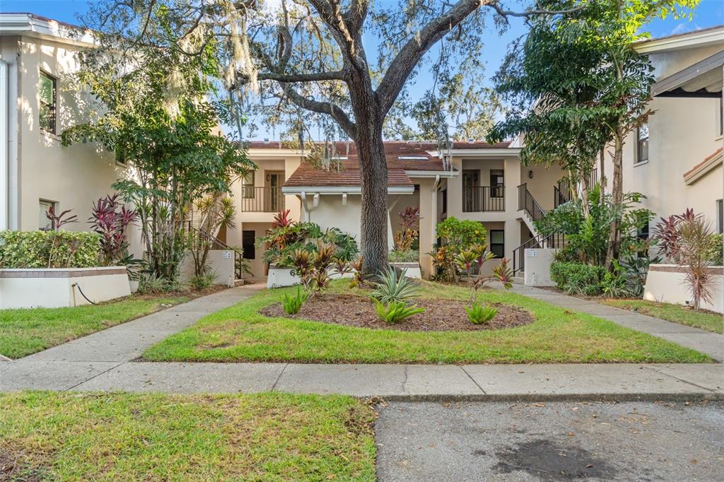 A two-story apartment building exterior features a central tree, landscaped garden, and concrete walkways — 300 S FLORIDA AVENUE UNIT 600F, TARPON SPRINGS, FL