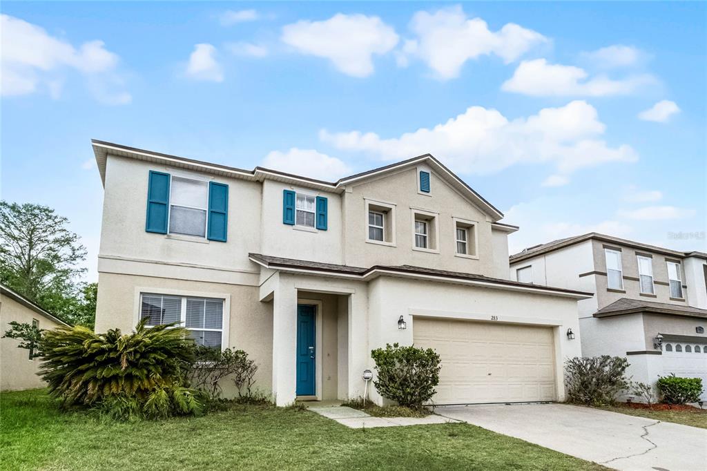 A two-story suburban house with a beige stucco exterior, blue shutters, and a two-car garage — 283 WILLOW VIEW DRIVE, DAVENPORT, FL