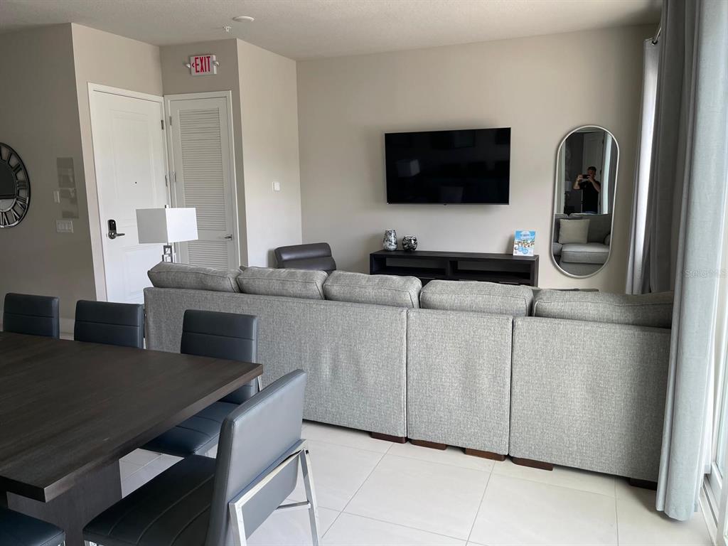 A living room features a grey sectional sofa, a wall-mounted television, and a dining area — 7770 SANDY RIDGE DRIVE UNIT 145, REUNION, FL