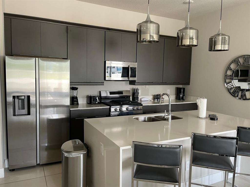A modern kitchen features dark gray cabinetry, stainless steel appliances, and a large quartz island — 7770 SANDY RIDGE DRIVE UNIT 145, REUNION, FL