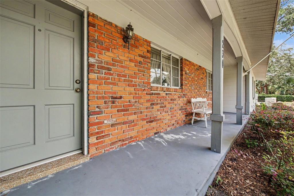 A gray front door opens onto a covered porch with a brick wall and bench — 230 S CRYSTAL DRIVE, SANFORD, FL