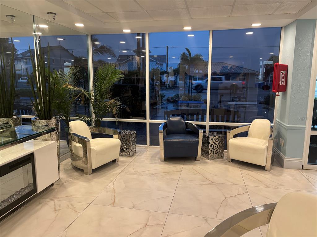 A modern lobby features three armchairs, marble-look tile flooring, and large windows overlooking a street — 9980 GULF BOULEVARD UNIT 317, ST PETERSBURG, FL