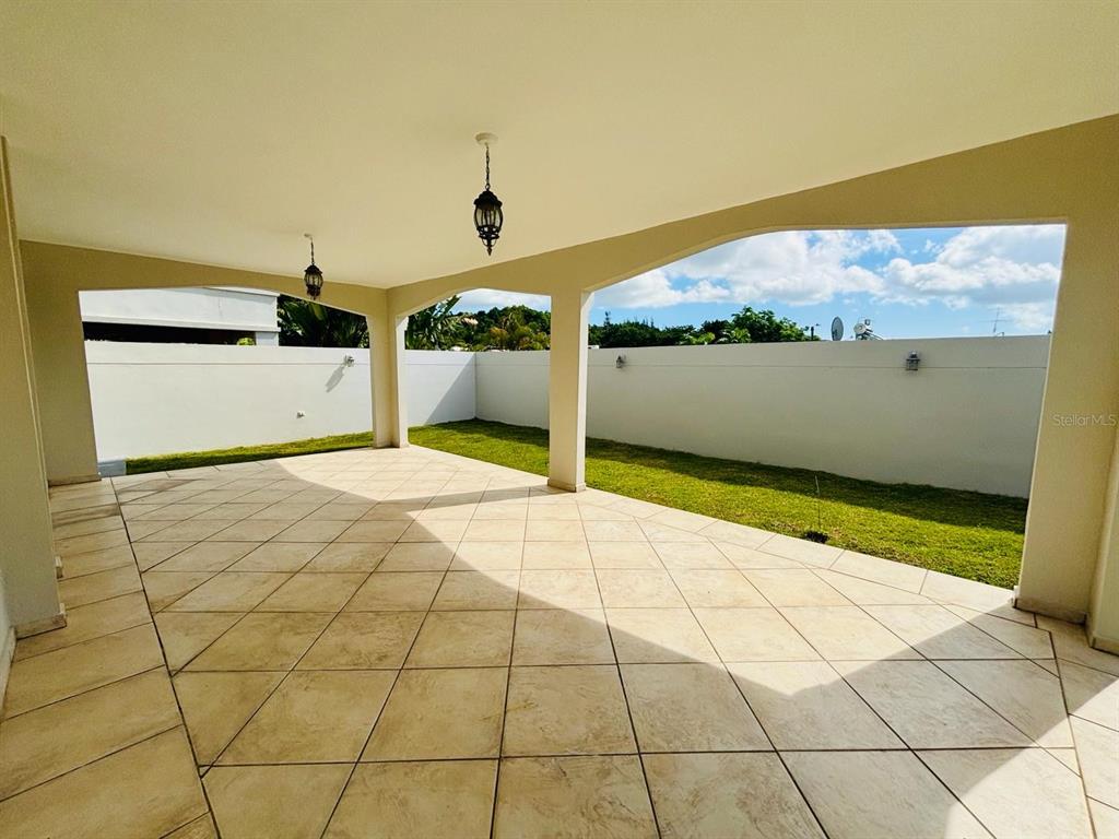 A covered patio with tiled flooring overlooks a grassy backyard enclosed by a white wall — Plaza de las Fuentes PLAZA DE LAS FUENTES, TOA ALTA, PR