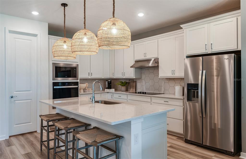 A modern kitchen features white cabinetry, a quartz-topped island, stainless steel appliances, and woven pendant lights — 8081 SW 45TH COURT ROAD, OCALA, FL