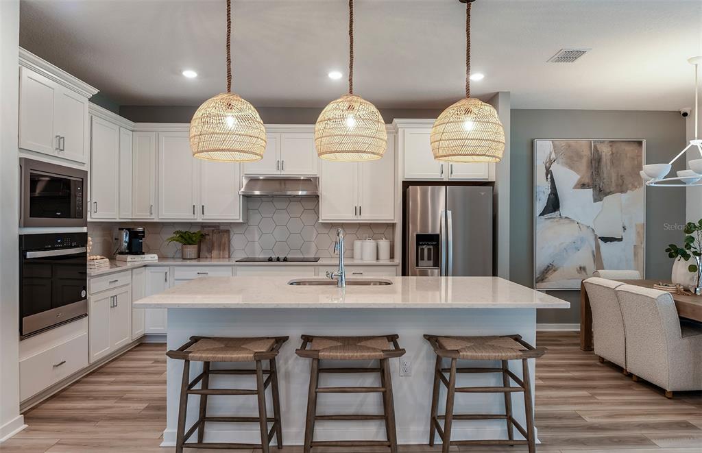 A modern kitchen features white cabinets, a quartz island with three stools, and woven pendant lights — 8081 SW 45TH COURT ROAD, OCALA, FL