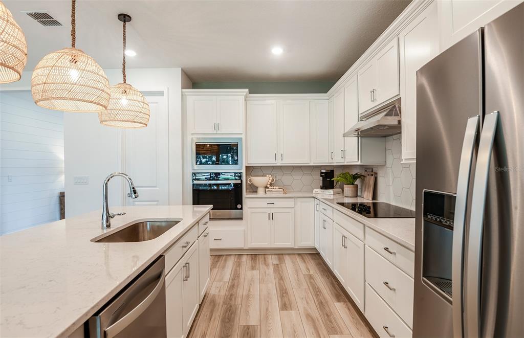 A modern kitchen features white cabinets, quartz countertops, stainless steel appliances, and woven pendant lights — 8081 SW 45TH COURT ROAD, OCALA, FL