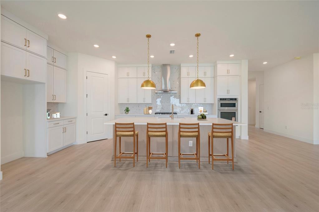 A modern kitchen features white cabinetry, a large central island with four chairs, and pendant lighting — 17988 FOXTAIL LOOP, VENICE, FL