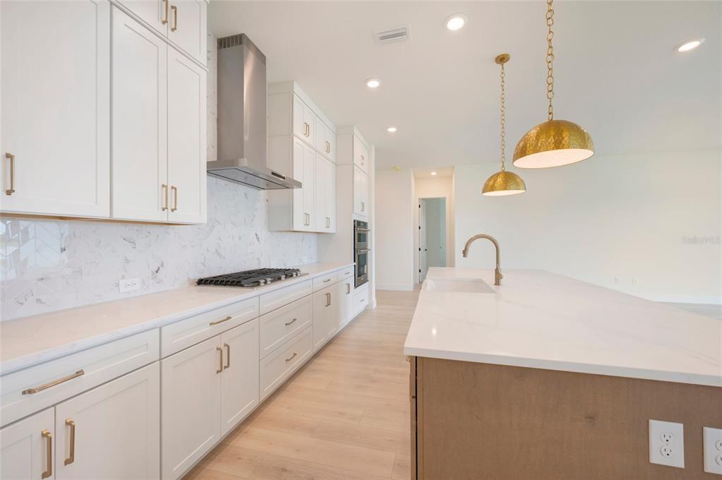 A modern kitchen features white cabinetry, a marble backsplash, a large island, and gold lighting — 17988 FOXTAIL LOOP, VENICE, FL